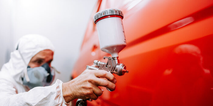 mechanic worker painting a car in a special painting box, wearing a full body costume and protection gear